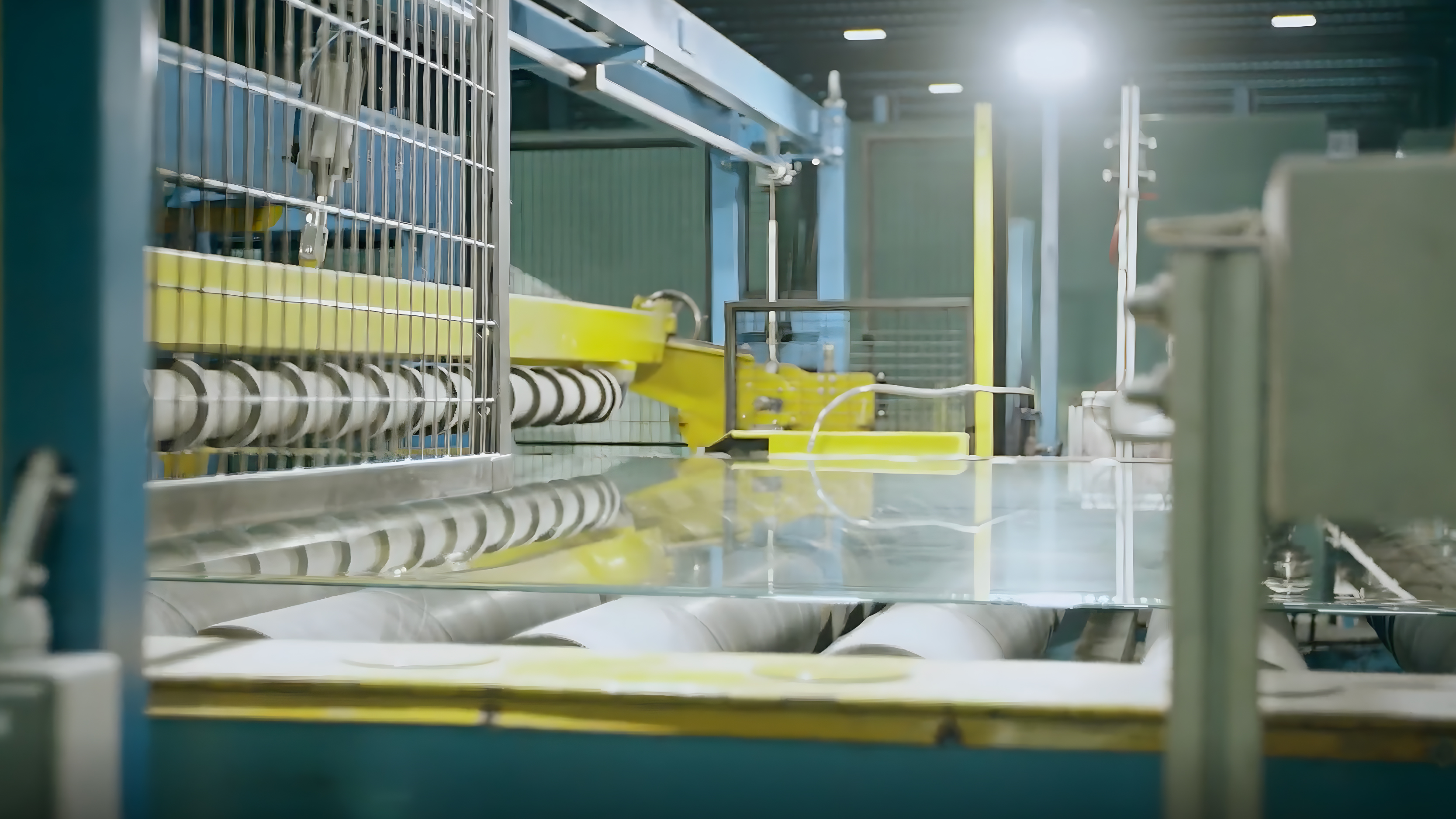 Factory scene with yellow and blue conveyor machinery transporting clear glass sheets through a production line.