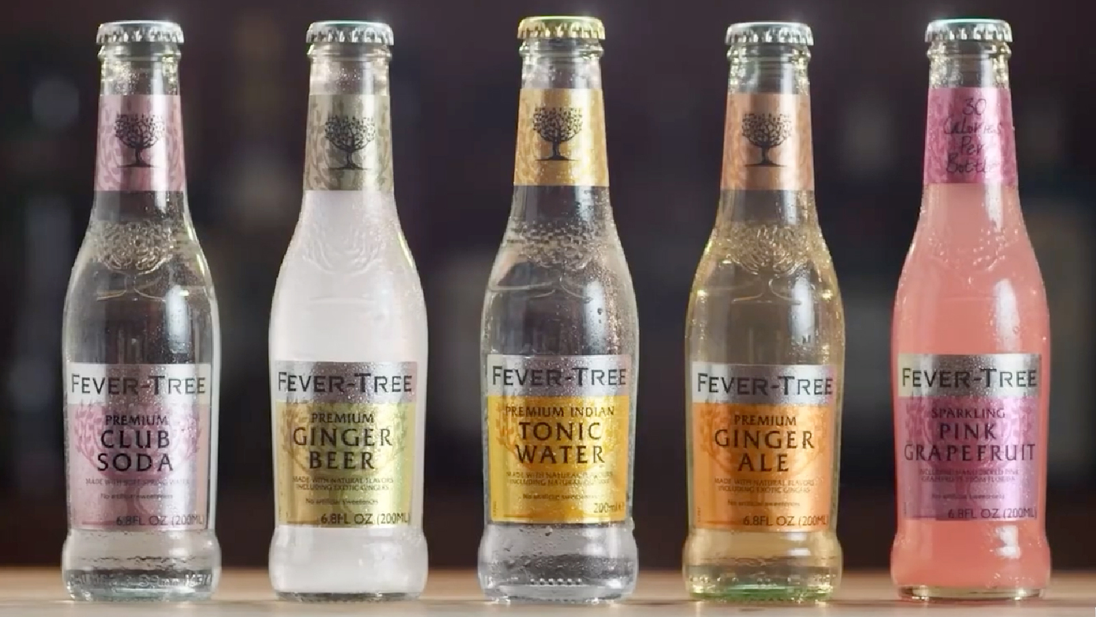 Lineup of five Fever-Tree bottles including Club Soda, Ginger Beer, Tonic Water, Ginger Ale, and Sparkling Pink Grapefruit, displayed with condensation.
