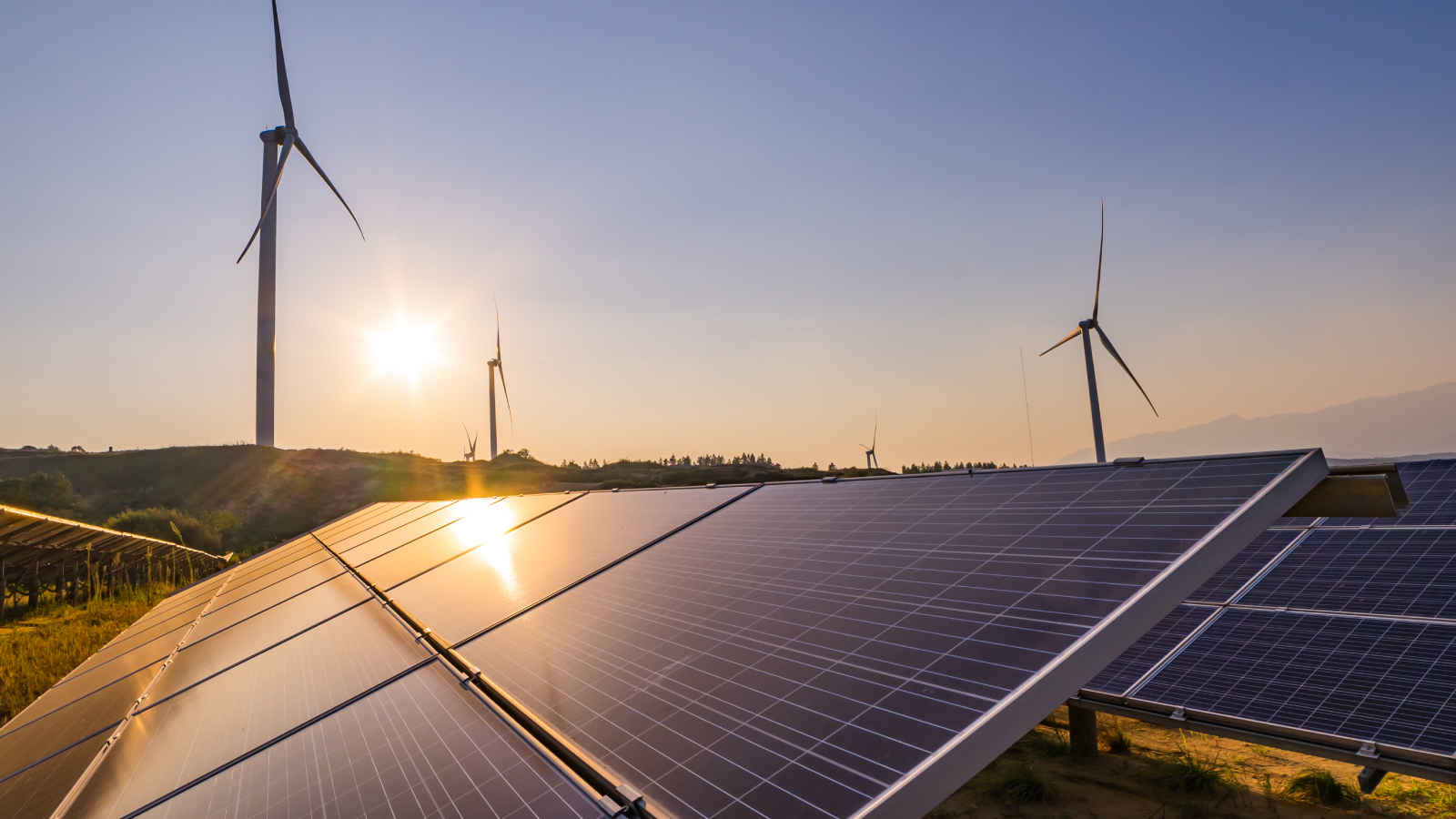 A scenic view of solar panels and wind turbines in a rural area at sunset, representing renewable energy sources.