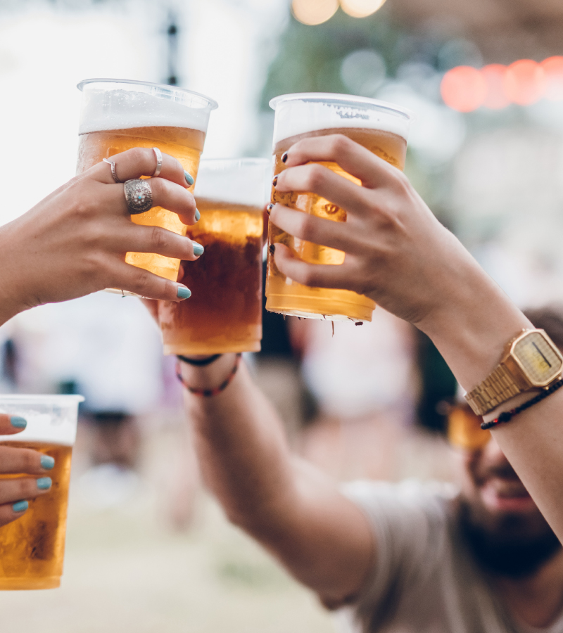A group of people clinking plastic cups of beer outdoors, celebrating in a lively, social setting.