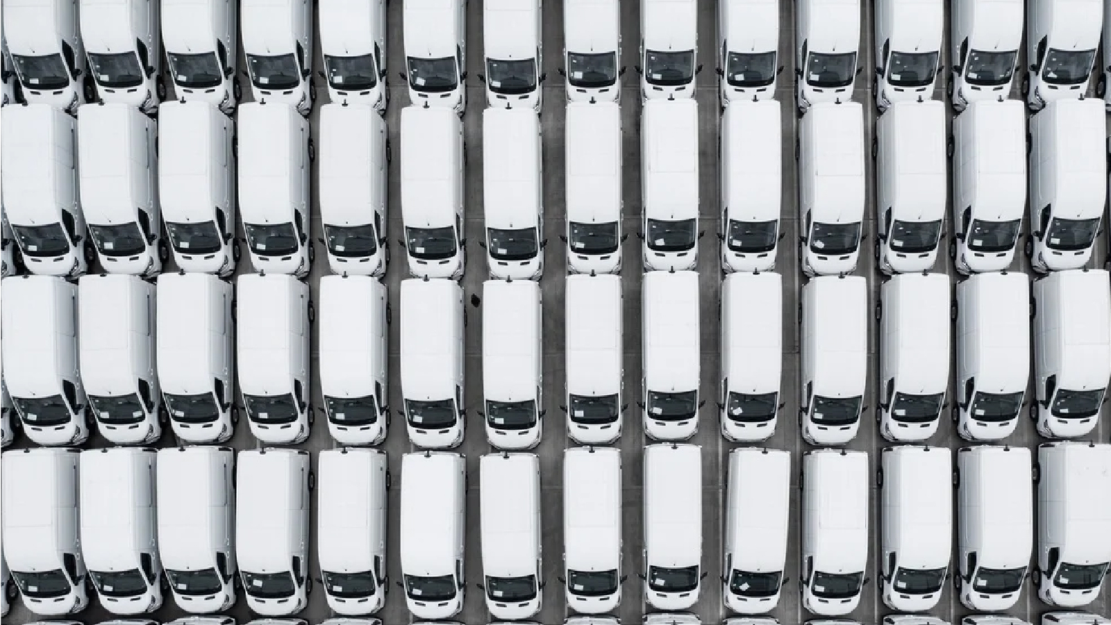 Overhead view of a large, tightly packed fleet of identical white vans parked in rows in a lot.