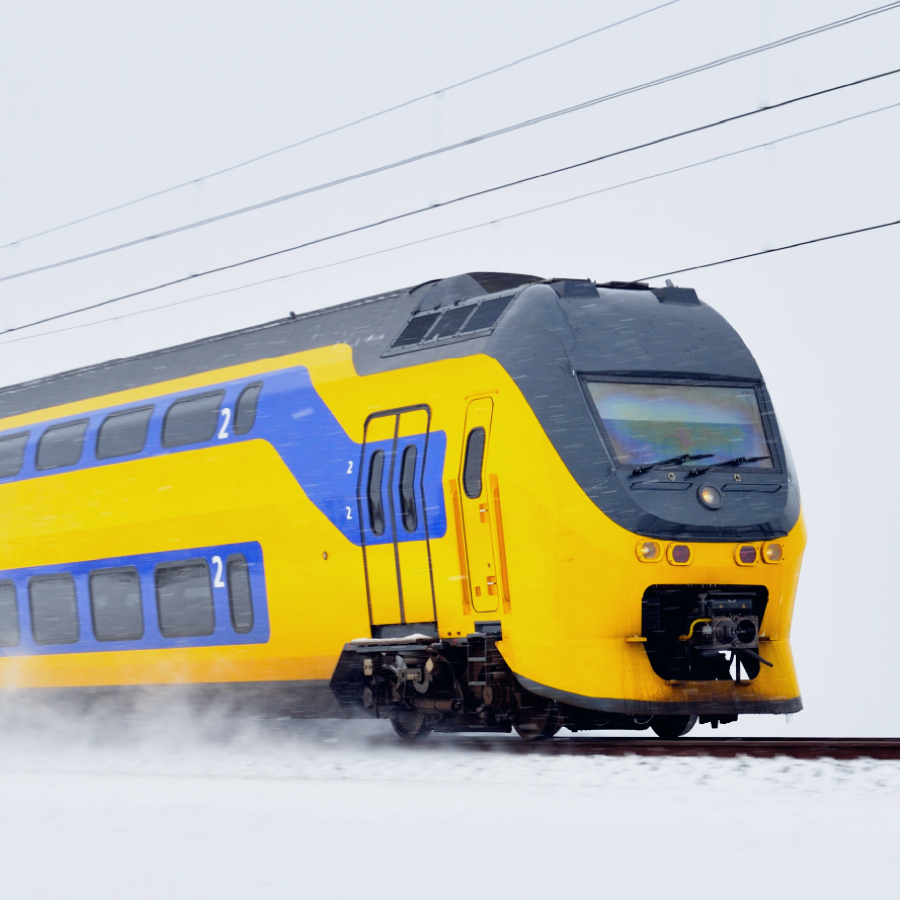 A bright yellow and blue Nederlandse Spoorwegen (NS) double-decker train speeding through snowy conditions, showcasing efficient railway transport in the Netherlands.