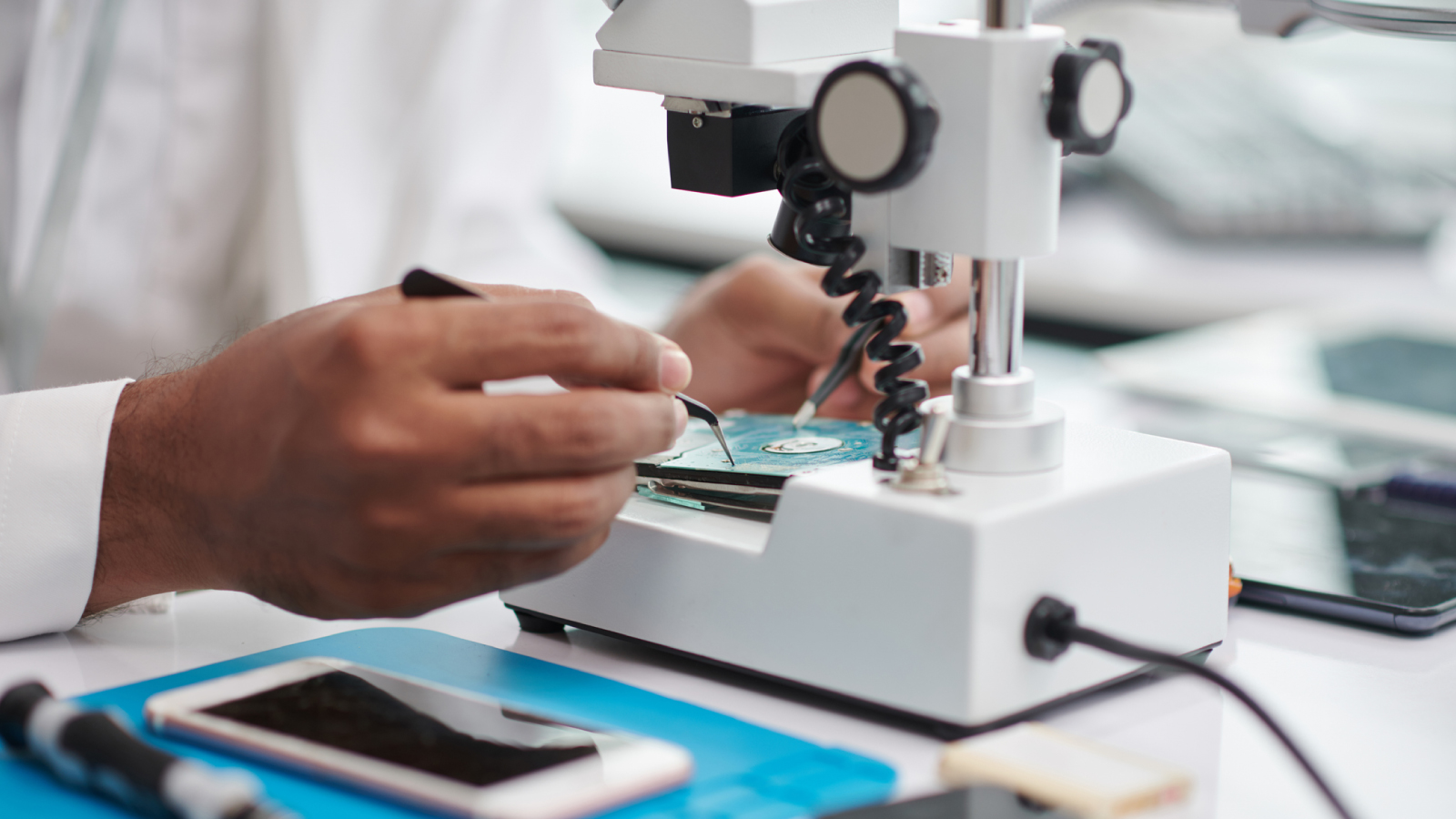 Close-up of a technician repairing a circuit board under a microscope.