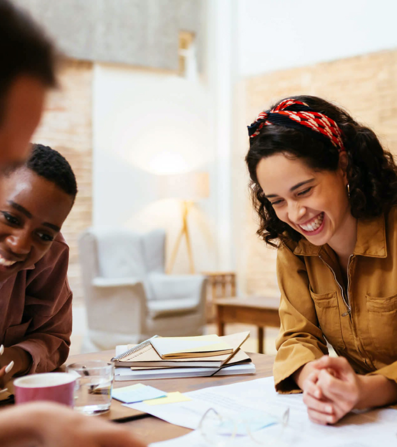 A group of young professionals gathered around a table, smiling and collaborating in a bright, modern workspace.