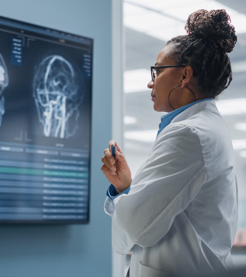 A focused doctor in a lab coat reviews brain scan images on a large monitor in a medical setting.