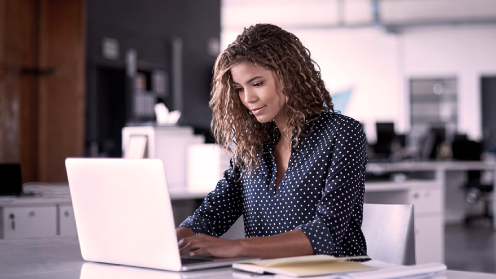Professional woman in a modern office intently using a laptop, reflecting secure, data‑driven work.