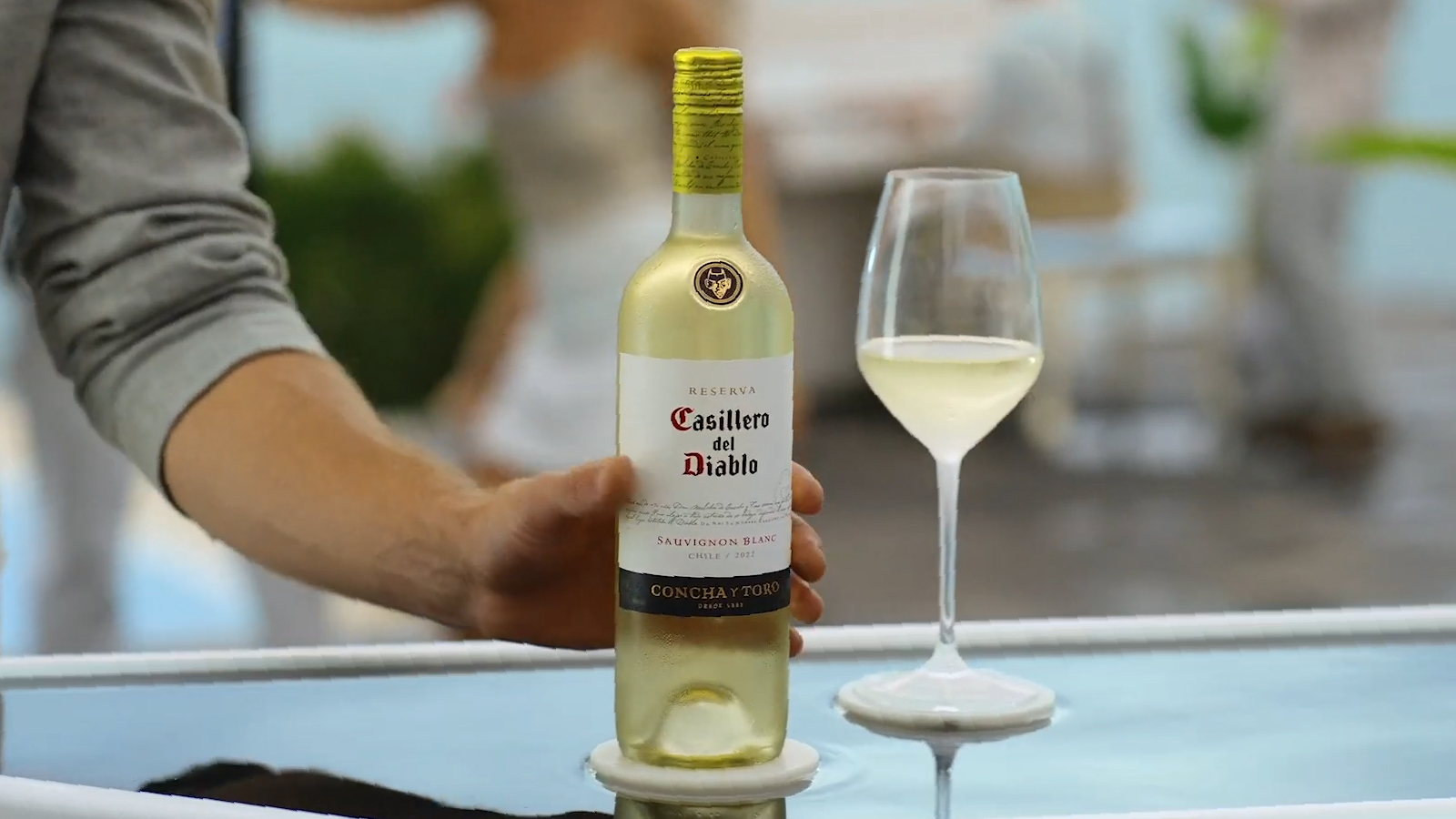 Man's arm grabbing a bottle of white wine next to a glass filled with white wine. 