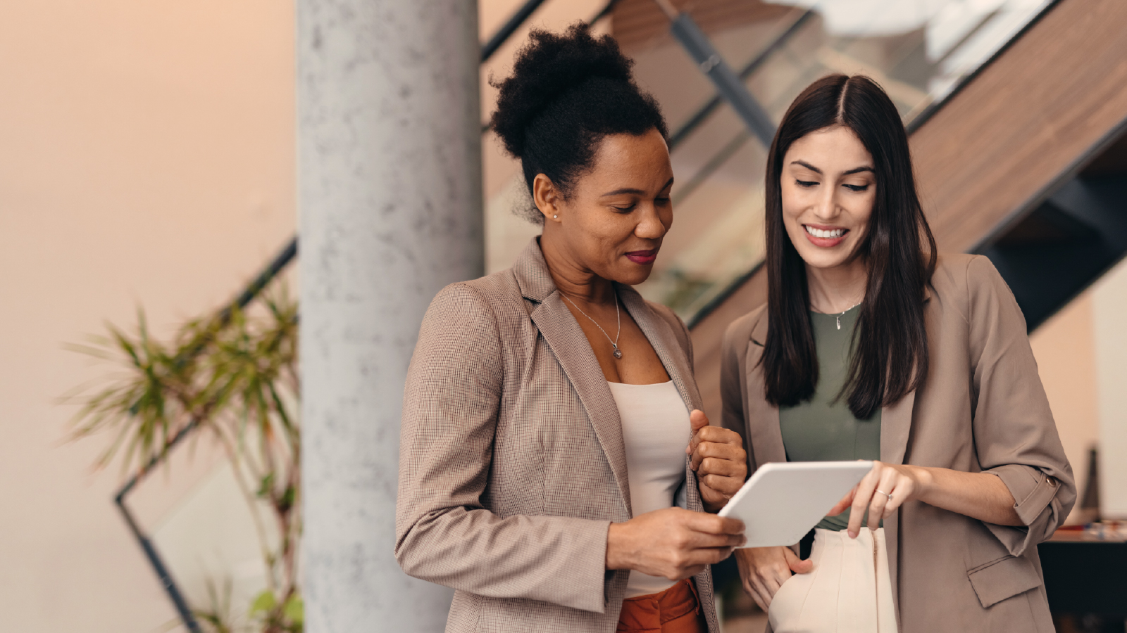 Two women in an office smiling and looking at a tablet together