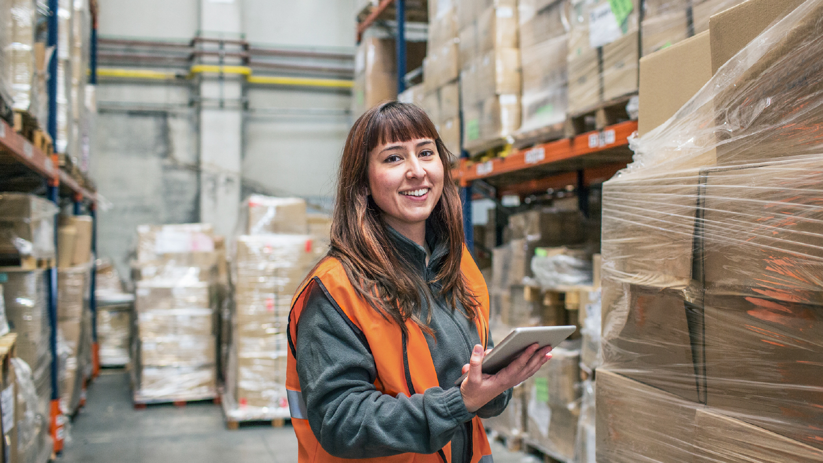 Image of a woman working in a warehouse smiling and holding a tablet
