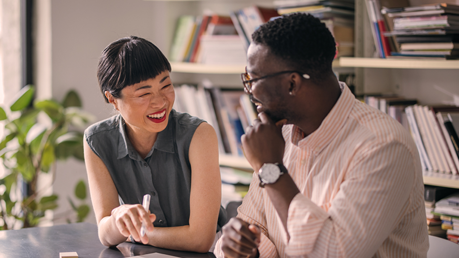 Two professionals sitting at a desk in an office, smiling and collaborating over documents, symbolizing teamwork and strategic discussion.