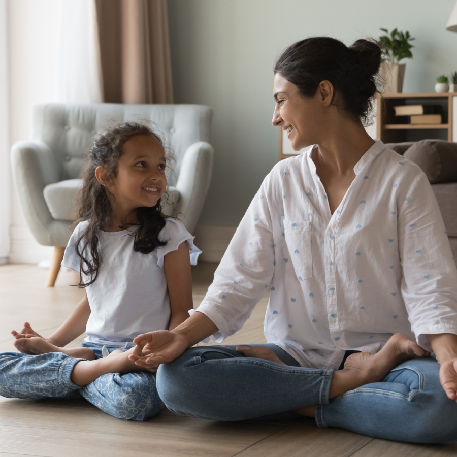 A woman and a little girl engaged in a yoga pose, sitting peacefully on a mat in a serene environment.