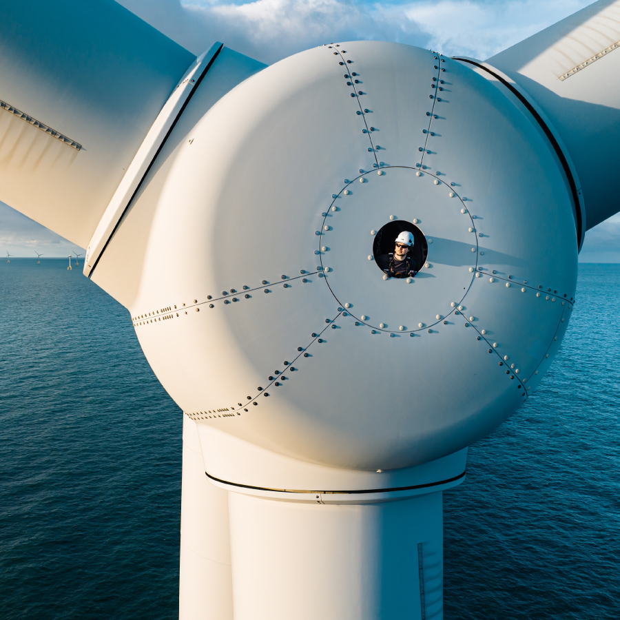 A figure is positioned on the summit of a wind turbine, gazing out over the expansive scenery below.