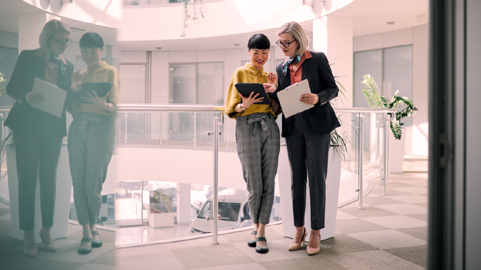 Two business professionals reviewing a tablet together in a modern office hallway with natural light.