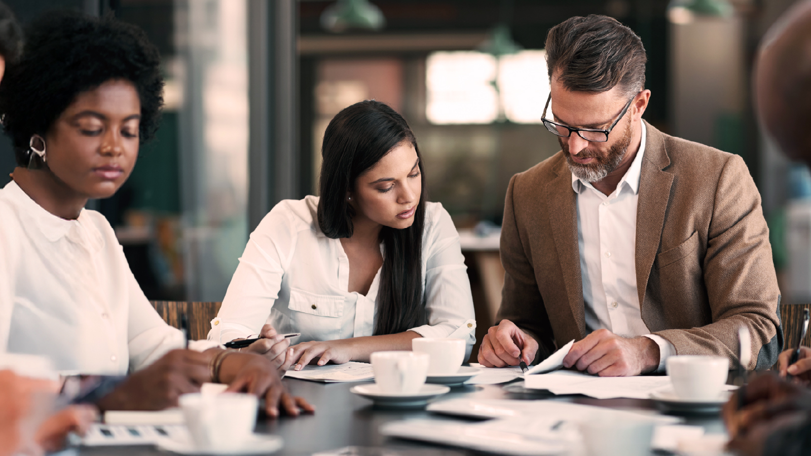 A diverse group of colleagues in a meeting room reviewing reports and collaborating on workforce planning, with coffee cups and papers spread across the table.