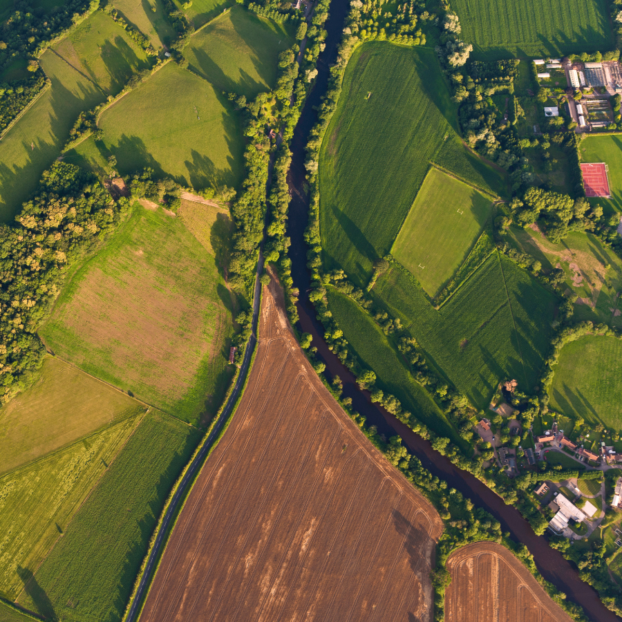Aerial view of a serene river winding through a lush green farm landscape, showcasing nature's beauty and agricultural harmony.