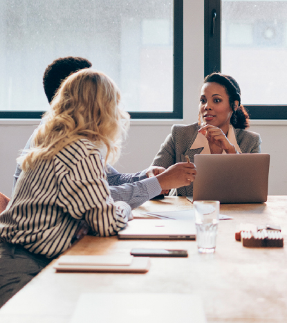 Three colleagues seated around a table in discussion, with one person speaking while others listen attentively