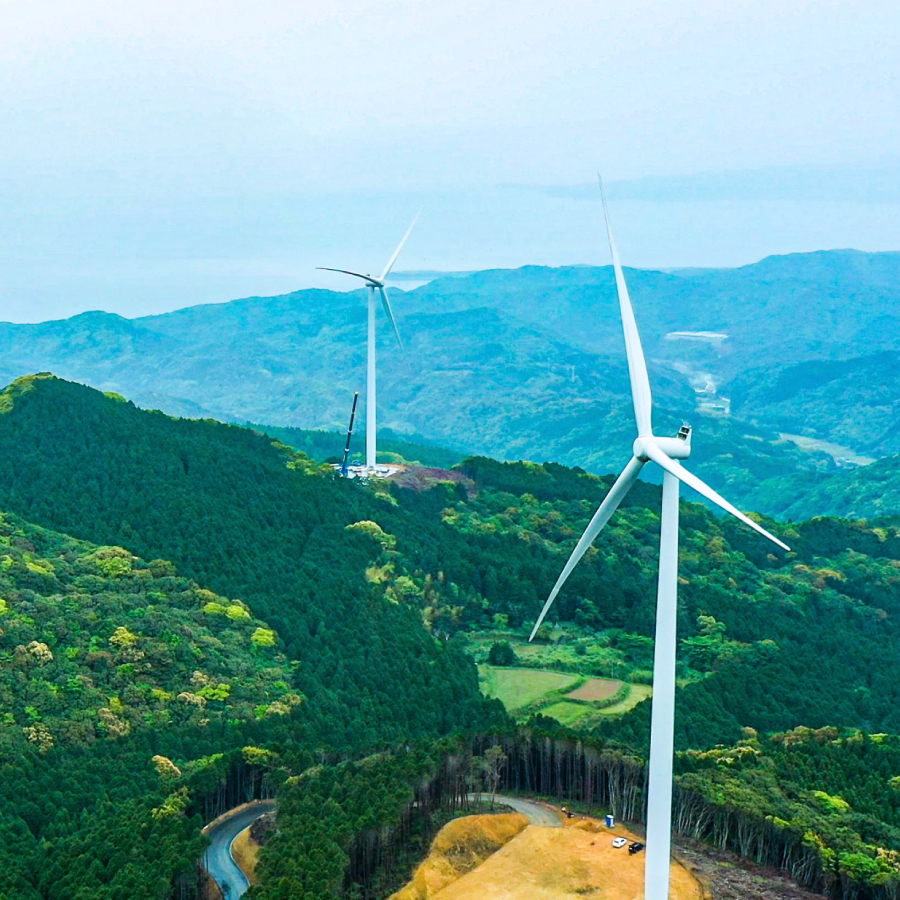 A scenic view of multiple wind turbines standing tall on a green hillside under a clear blue sky.