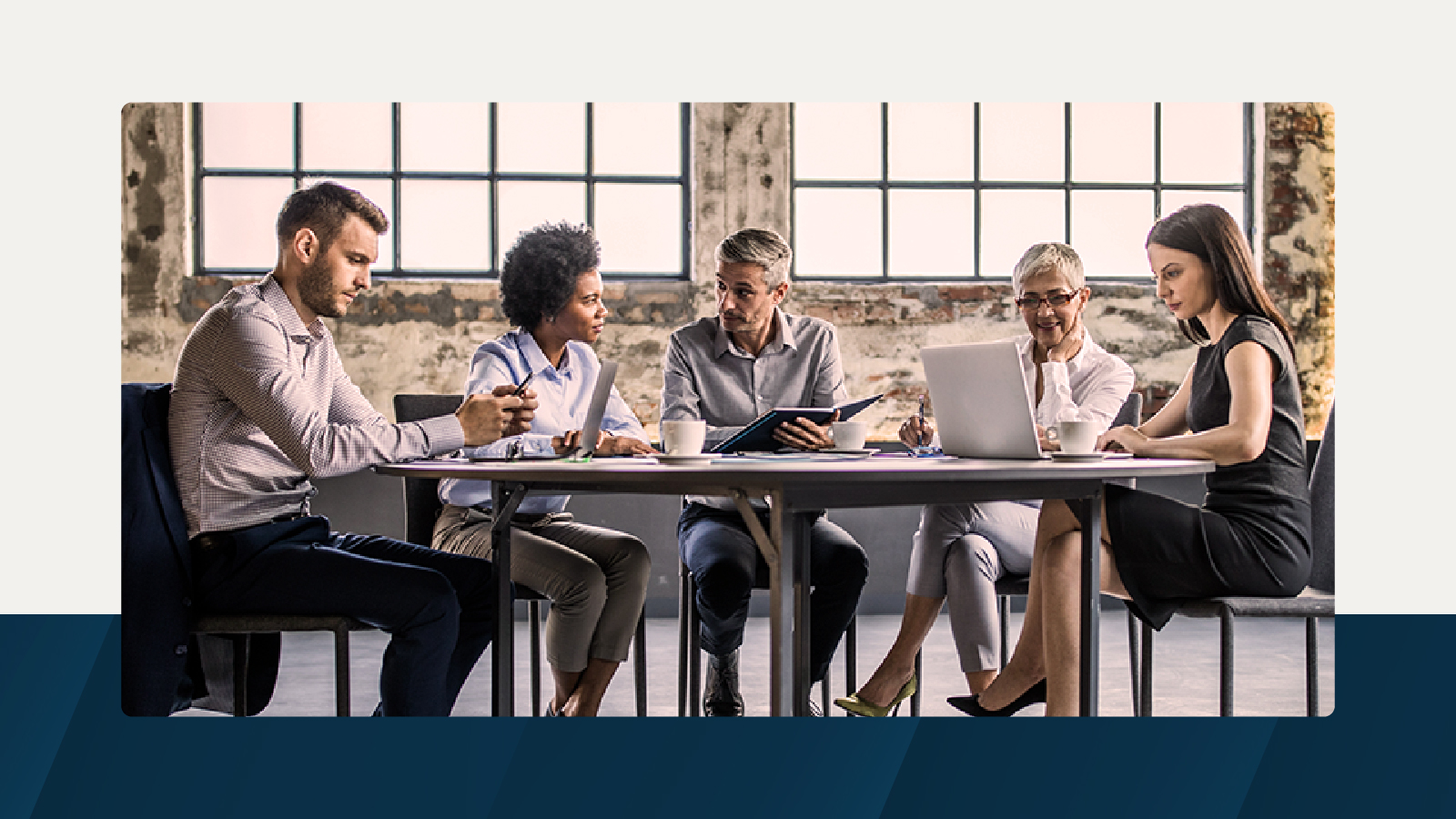 Five professionals collaborating at a meeting table in a modern industrial-style office.