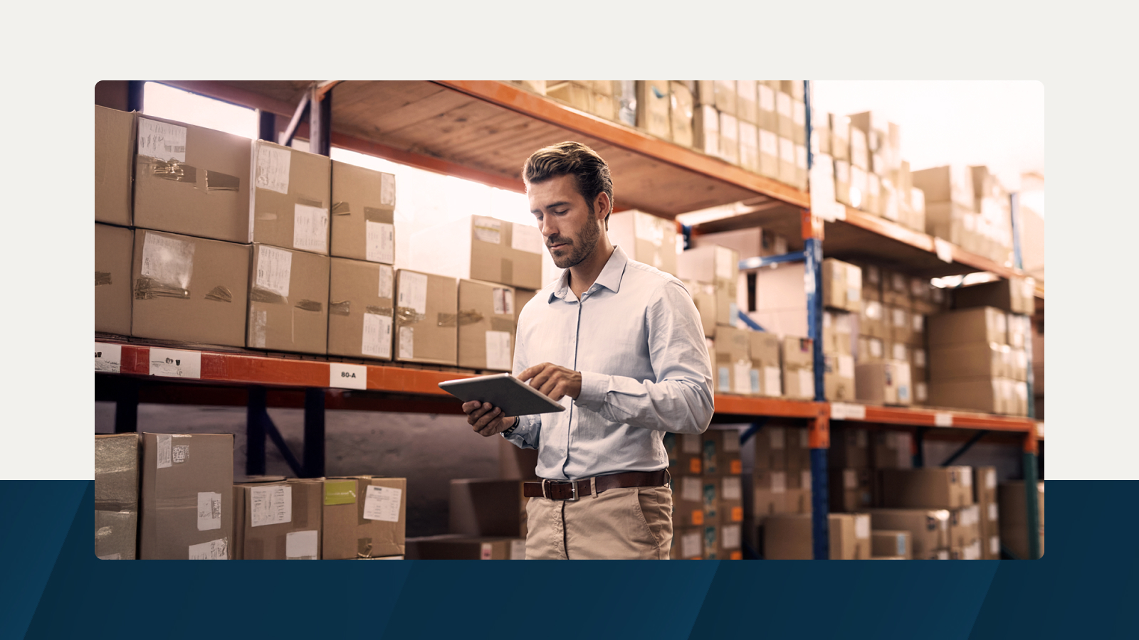 A supply chain professional reviewing inventory data on a tablet in a warehouse environment.