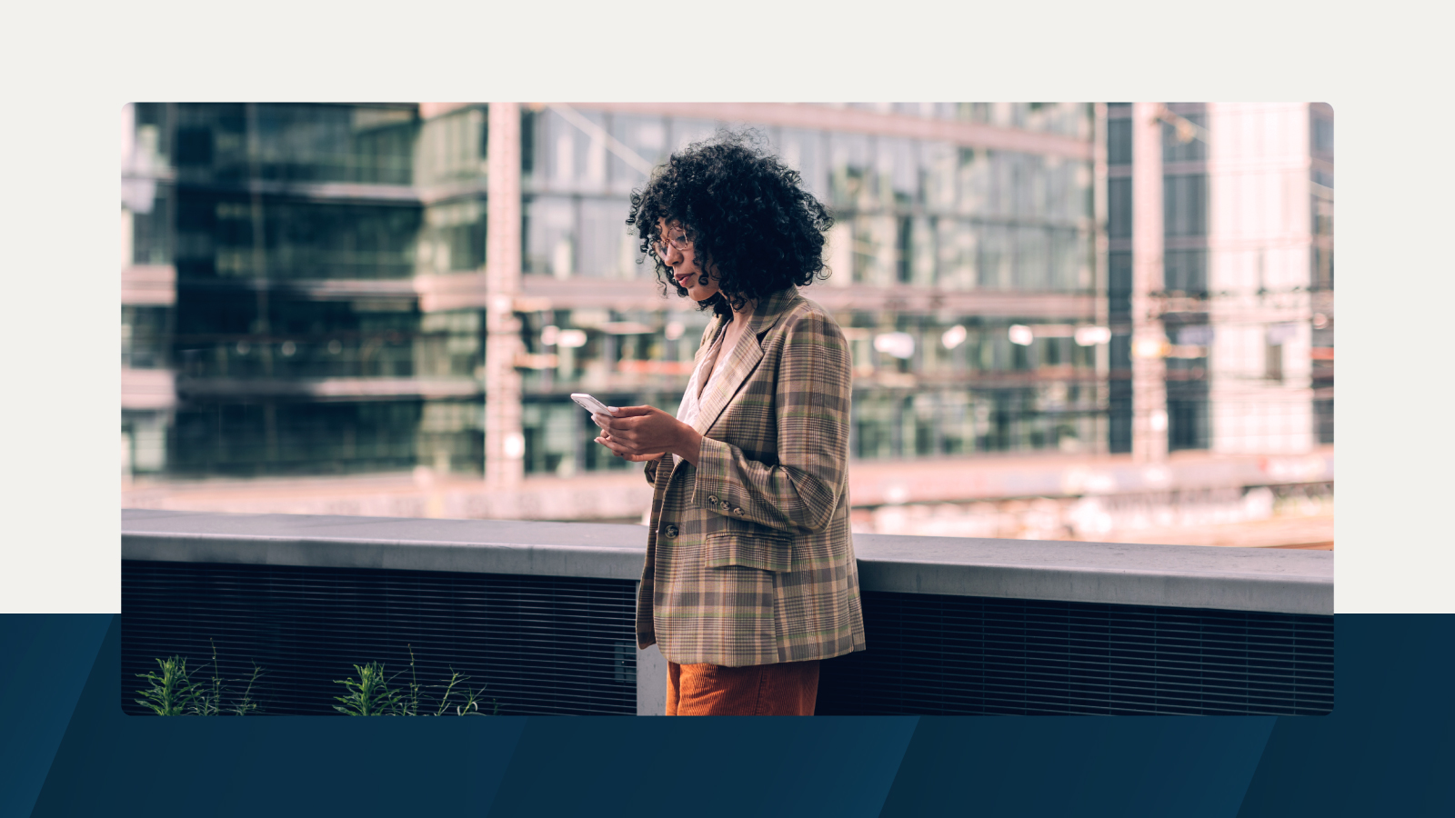 A professional stands outdoors near an urban office building, focused on a smartphone