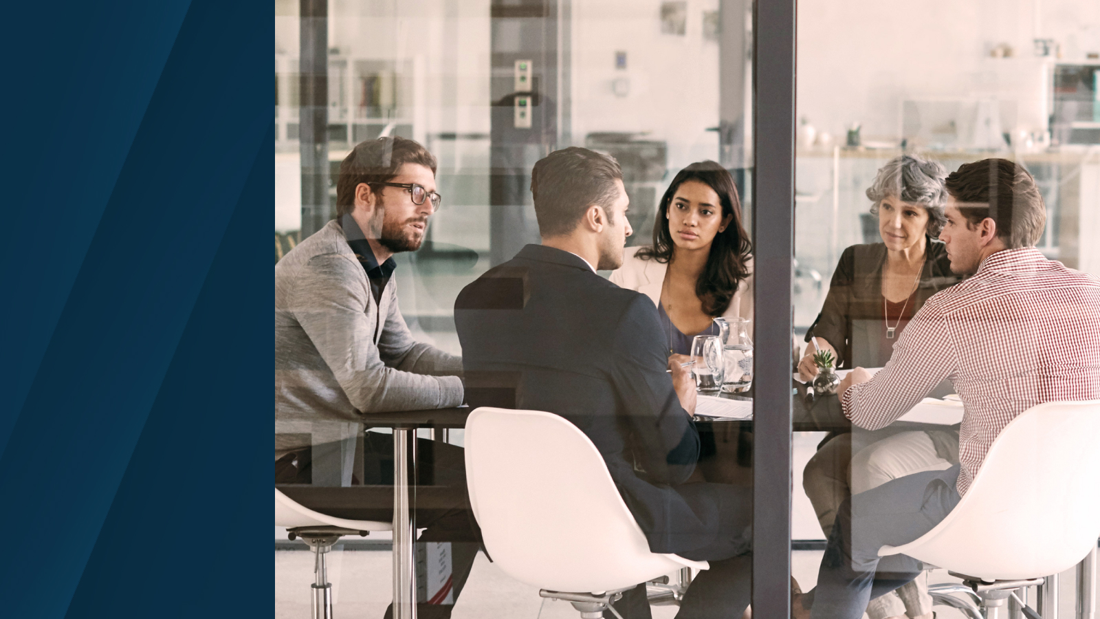 A group of professionals engaged in a discussion inside a modern glass-walled conference room.