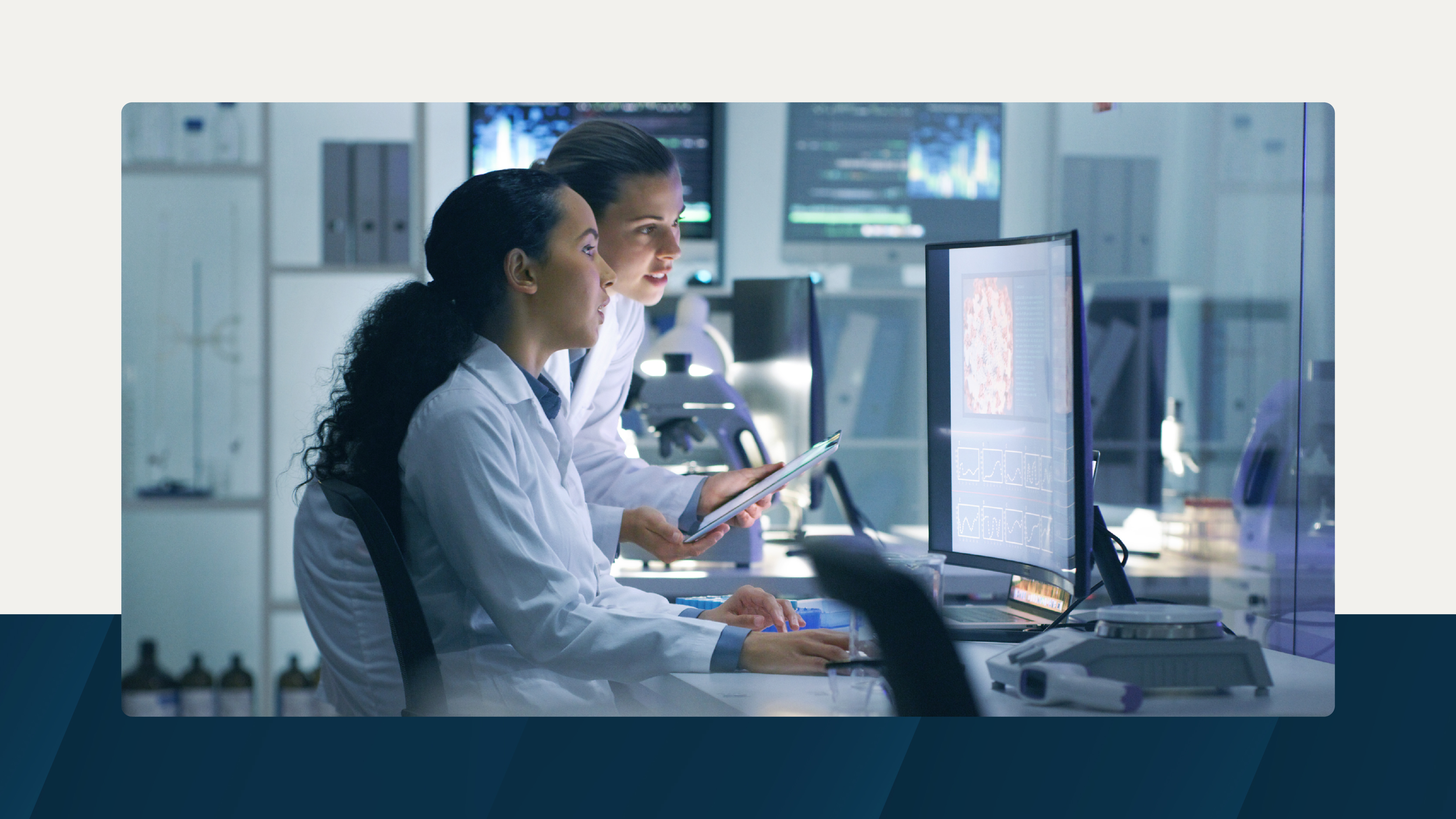 Two scientists in lab coats working together at a computer station in a modern laboratory, surrounded by monitors displaying scientific data.