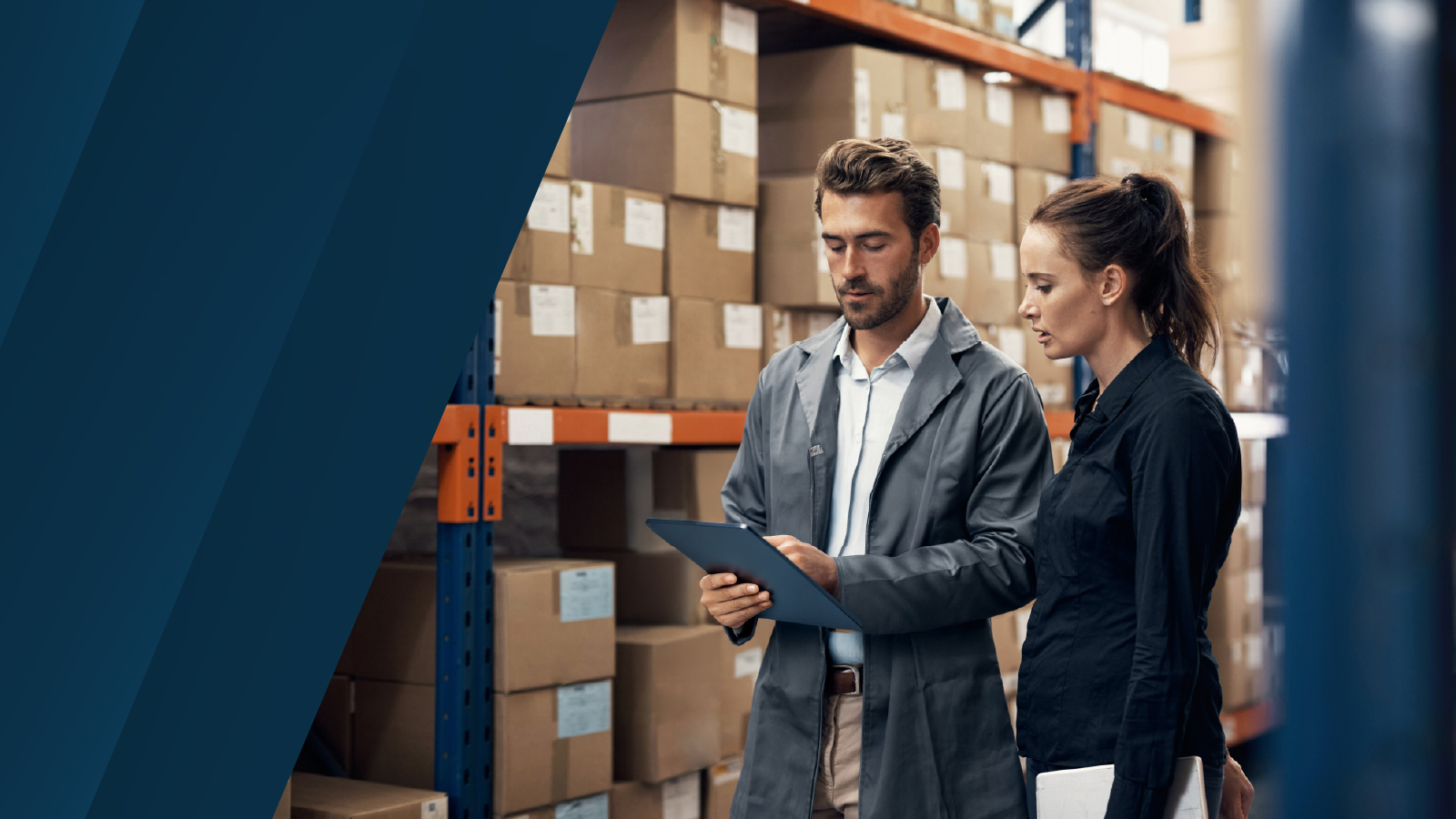 Two professionals standing in a warehouse, reviewing a tablet, with shelves of stacked cardboard boxes in the background, partially overlaid by a dark blue design element.
