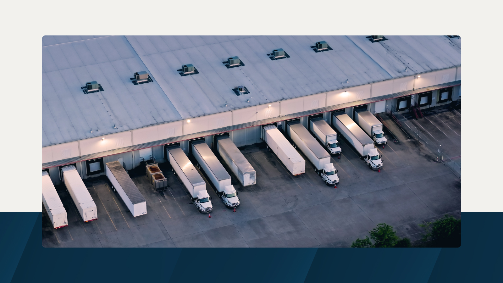 Aerial view of a warehouse loading dock with semi-trailers backed into bays, under soft evening lighting.