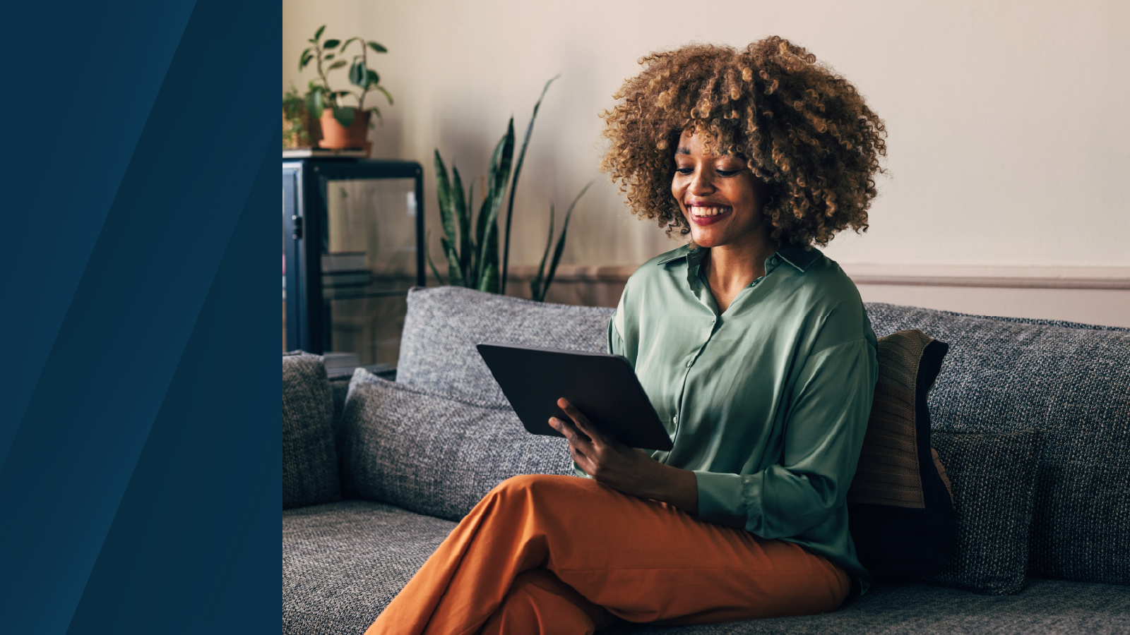 Woman smiling sitting on a couch looking at a tablet