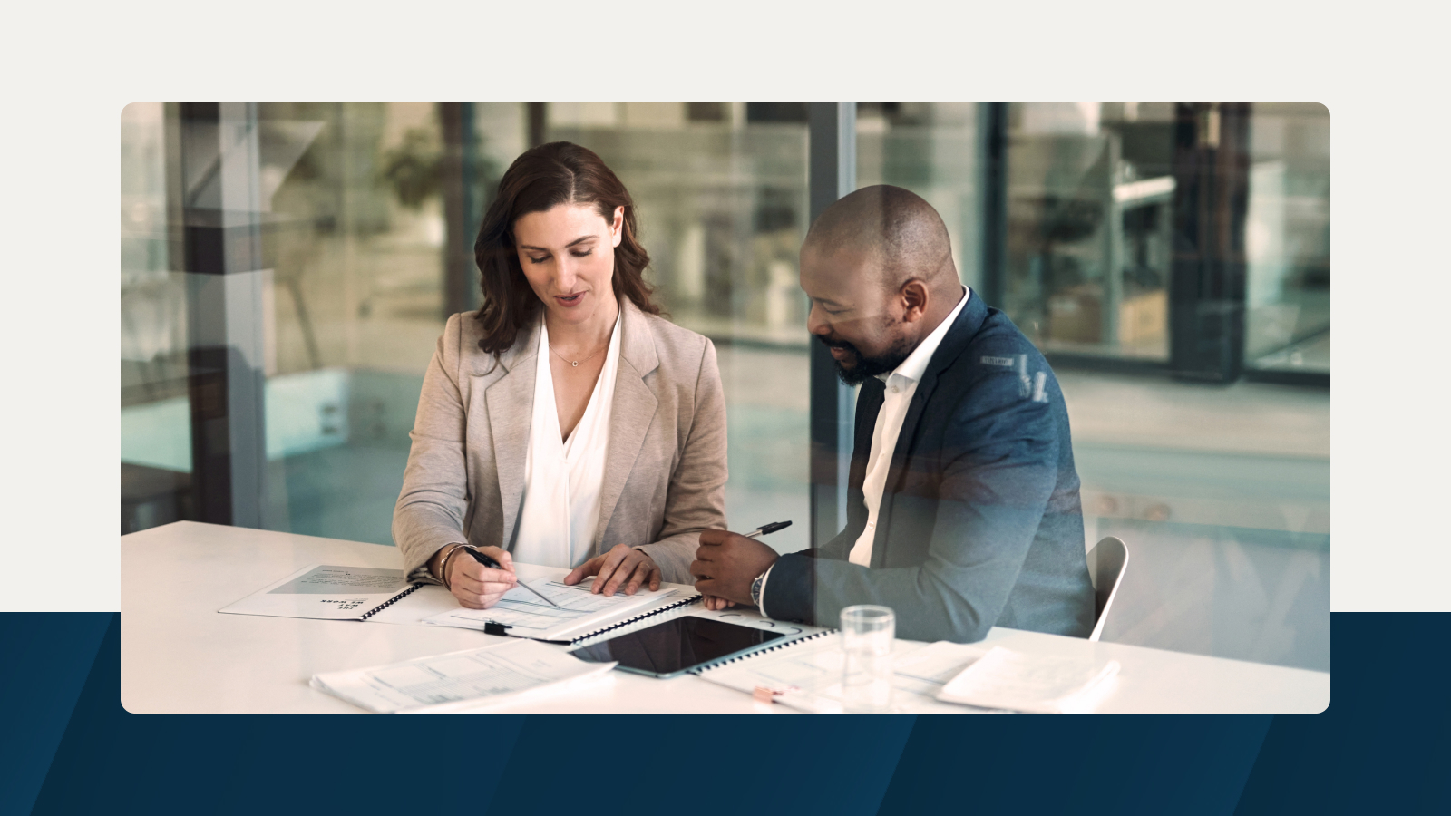 Two business professionals discussing long-range financial planning at a modern office table with documents and a tablet.