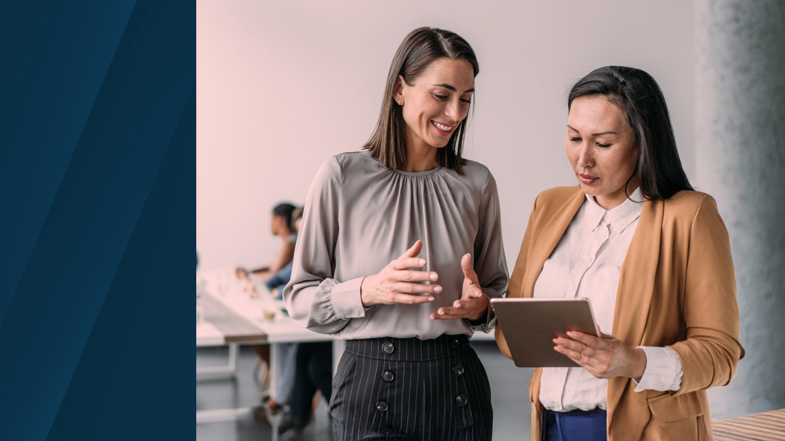Two professionals reviewing data on a tablet in a collaborative workspace, with a blurred background of a modern office setting.