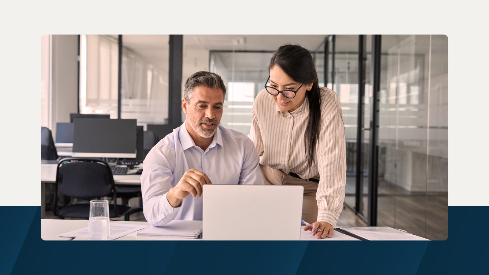 Two colleagues working together on a laptop in a modern office, discussing a project with focus and collaboration.