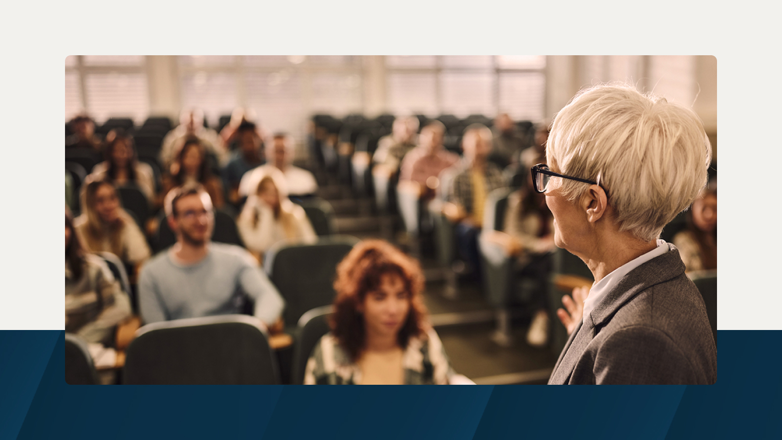 A university professor with short white hair and glasses engages with students in a lecture hall, symbolizing the importance of optimized learning spaces.