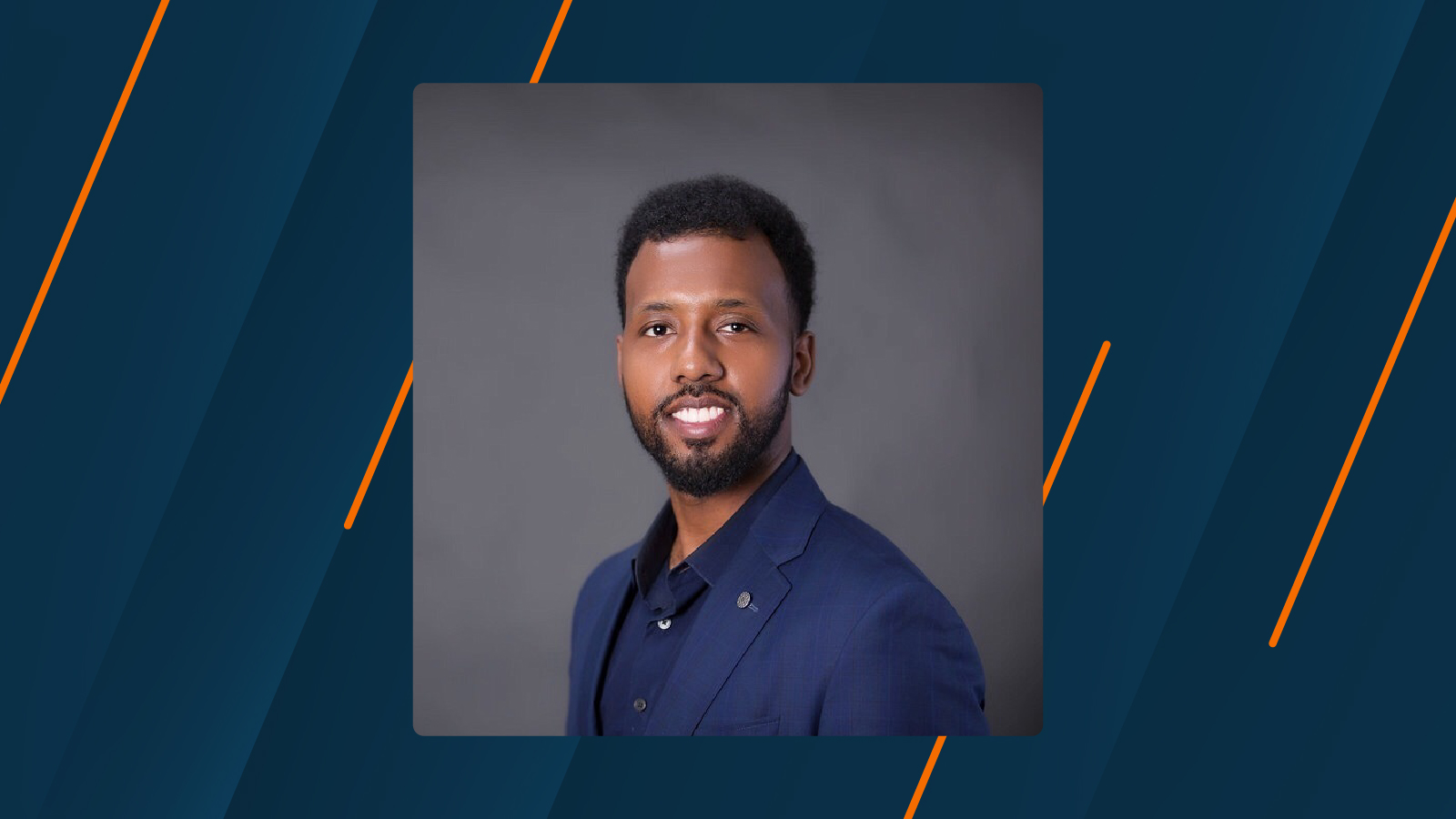 A professional headshot of a smiling man in a dark blue suit jacket against a gray background, with a patterned dark blue and orange background design.
