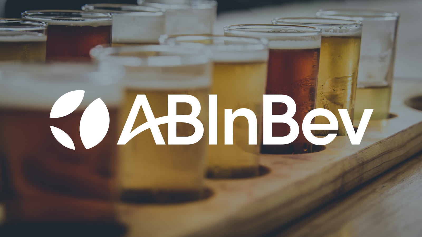 ABInBev Logo displayed center. White logo over a close-up of assorted beer glasses arranged on a wooden tray.