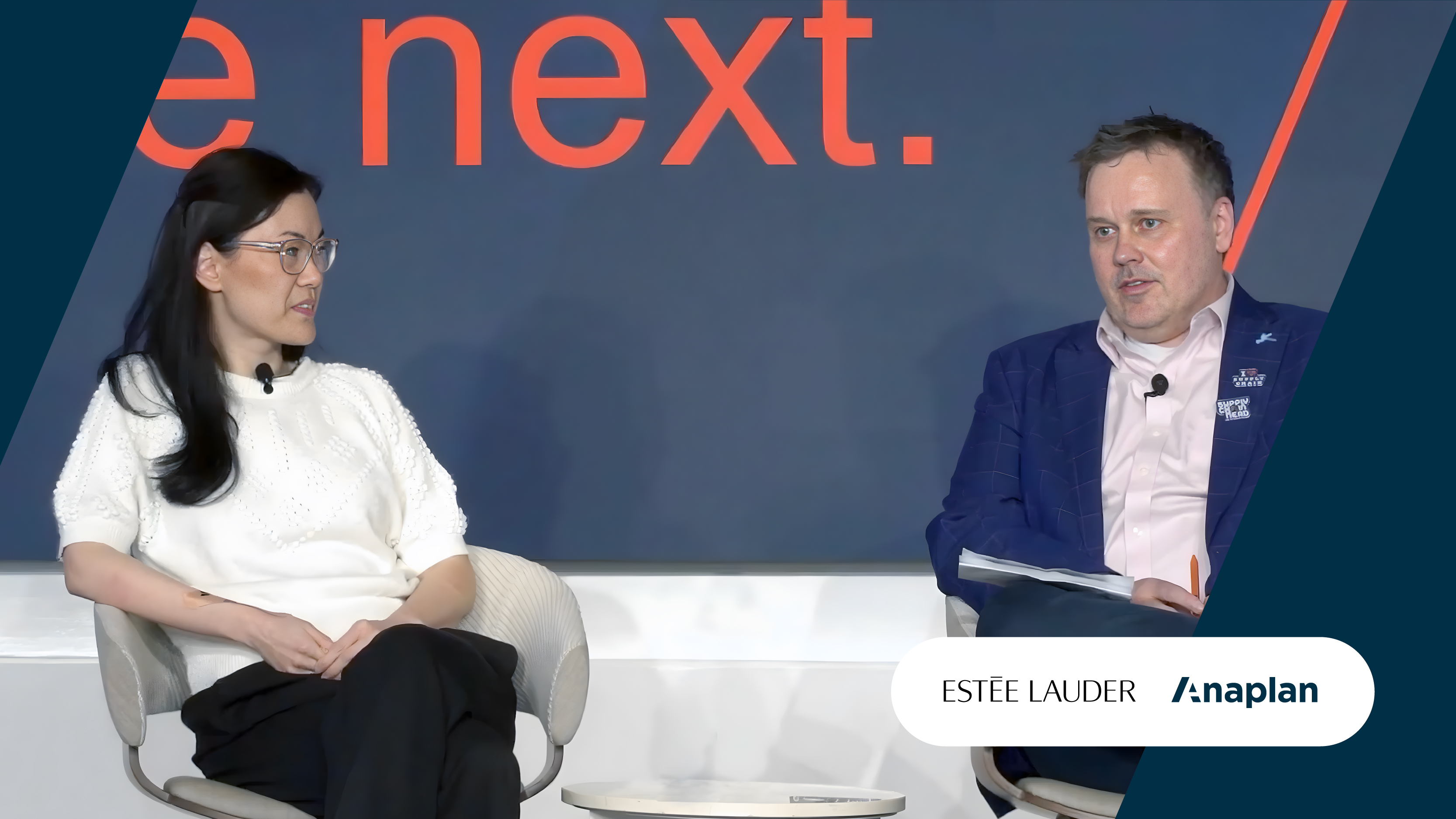 Estée Lauder and Anaplan Logos displayed bottom right. Two panelists seated in conversation on stage with a large orange text backdrop.