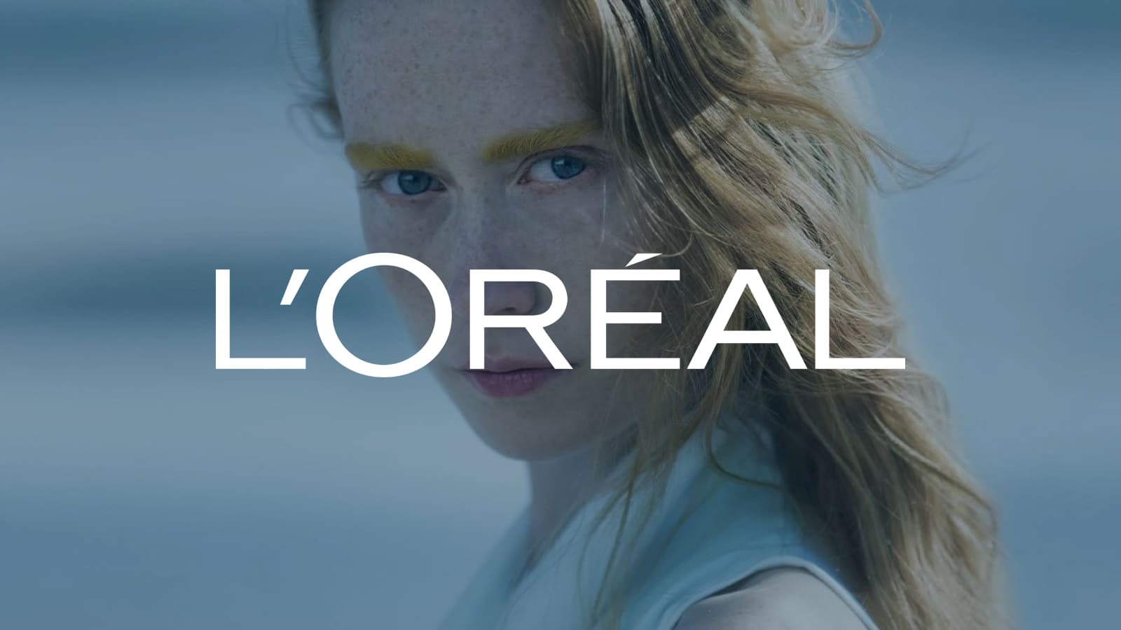 L'Oréal Logo displayed center. A close-up portrait of a woman with red hair and yellow eyebrows looking directly at the camera.