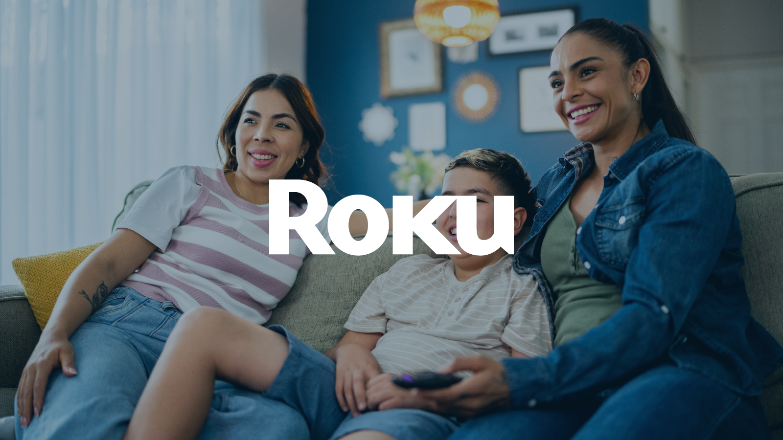 Roku logo displayed over a background image of two women and a boy sitting on a couch, smiling together in a cozy living room.